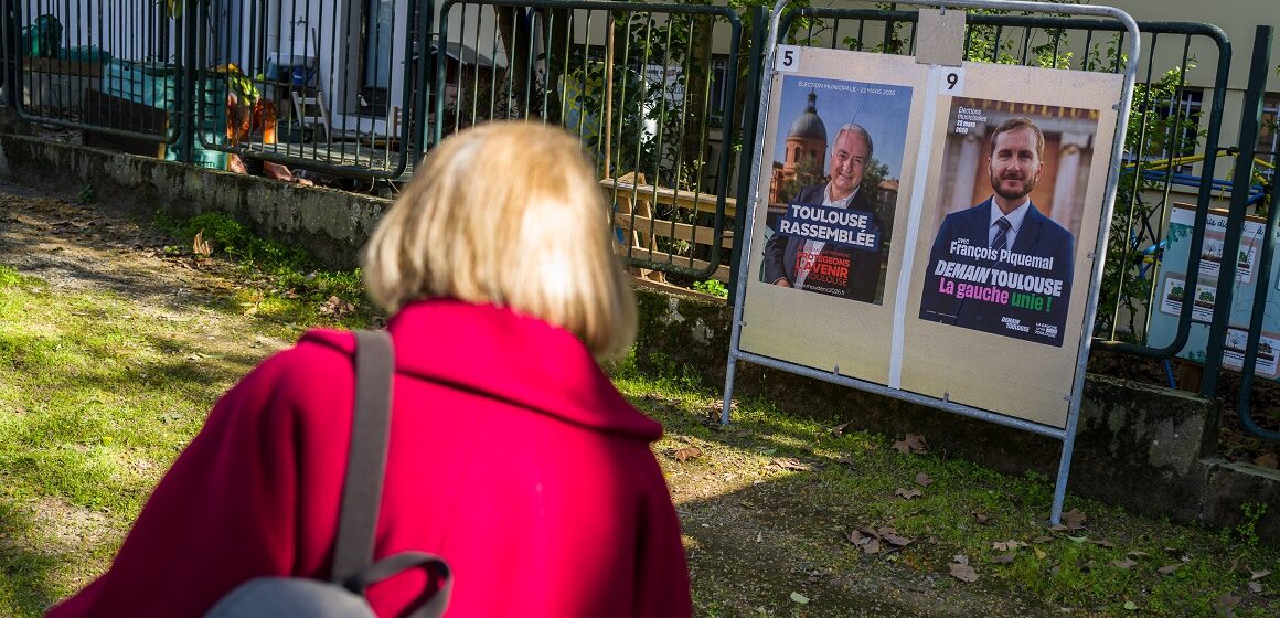 Toulouse, 20 mars 2026. Une personne regarde les panneaux électoraux en vue du second tour des élections municipales le 22 mars 2026 avec l’actuel Maire de Toulouse Jean Luc Moudenc (G) et Francois Piquemal pour LFI (D). Photo : Frédéric Scheiber / Hans Lucas via AFP